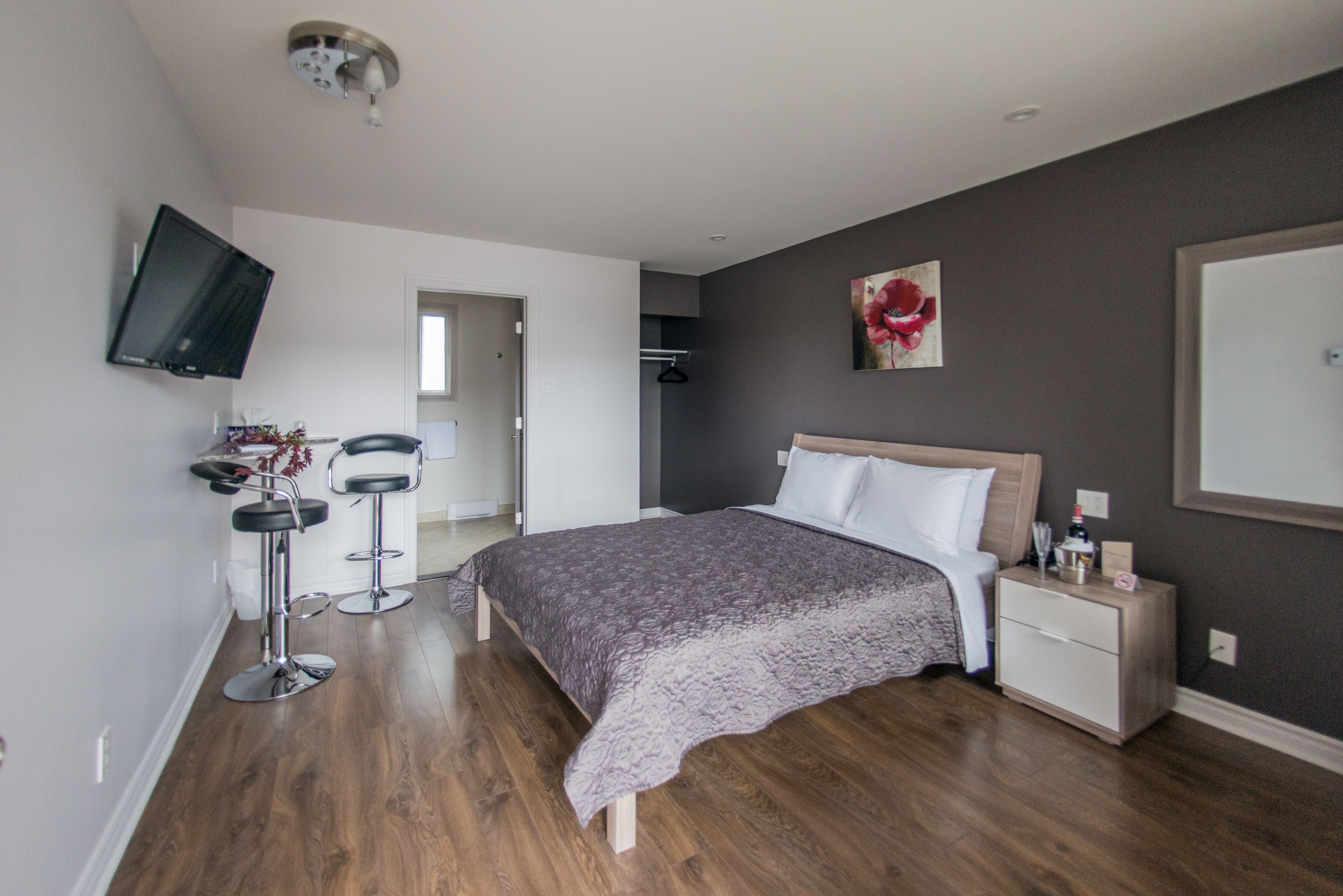 Une chambre à coucher moderne, dotée d’un grand lit, de tables de chevet et d’un téléviseur fixé au mur, ainsi que d’un couloir menant à une salle de bain.