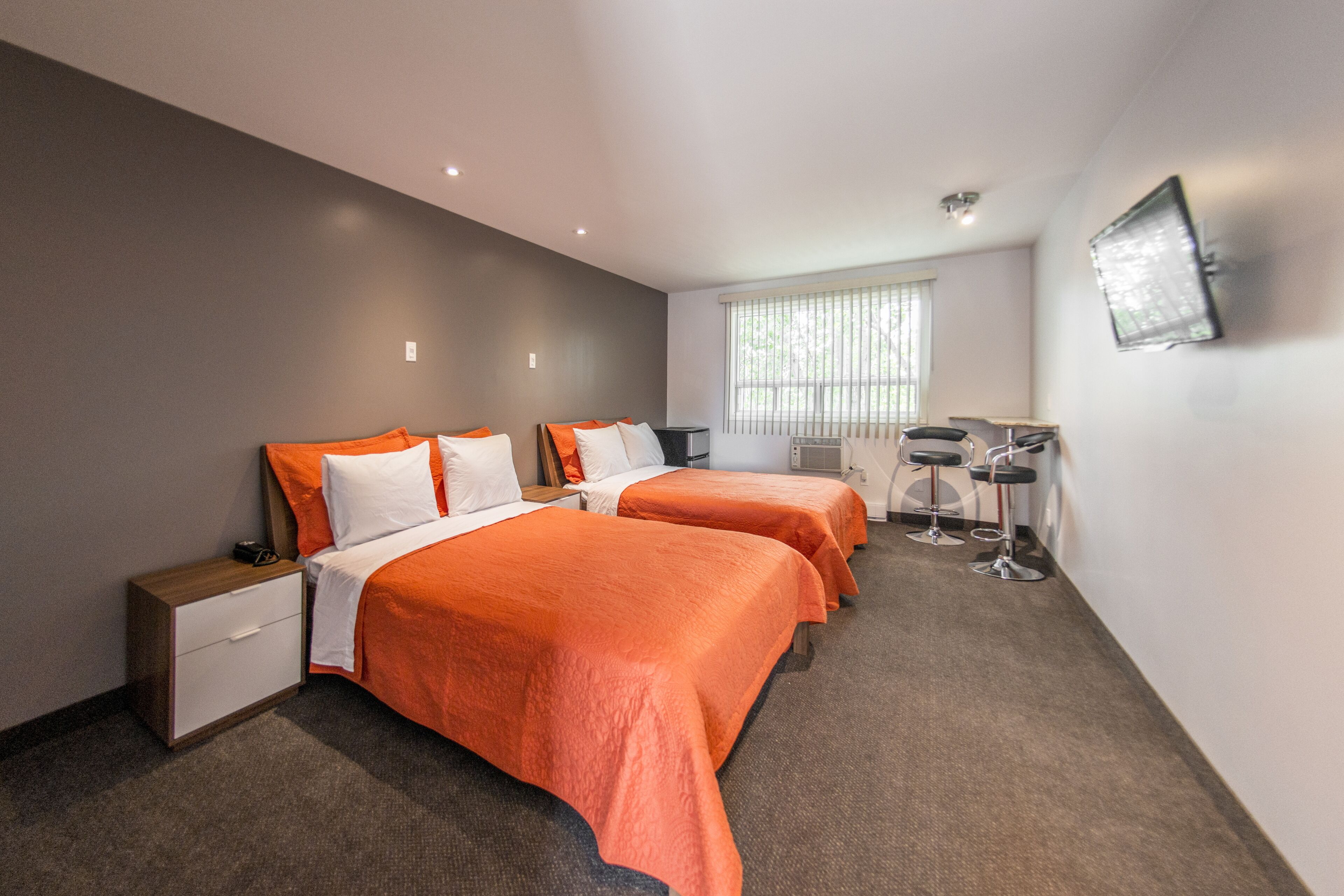 Une chambre d’hôtel avec deux lits, un bureau, une chaise, une télévision et une fenêtre avec des stores.