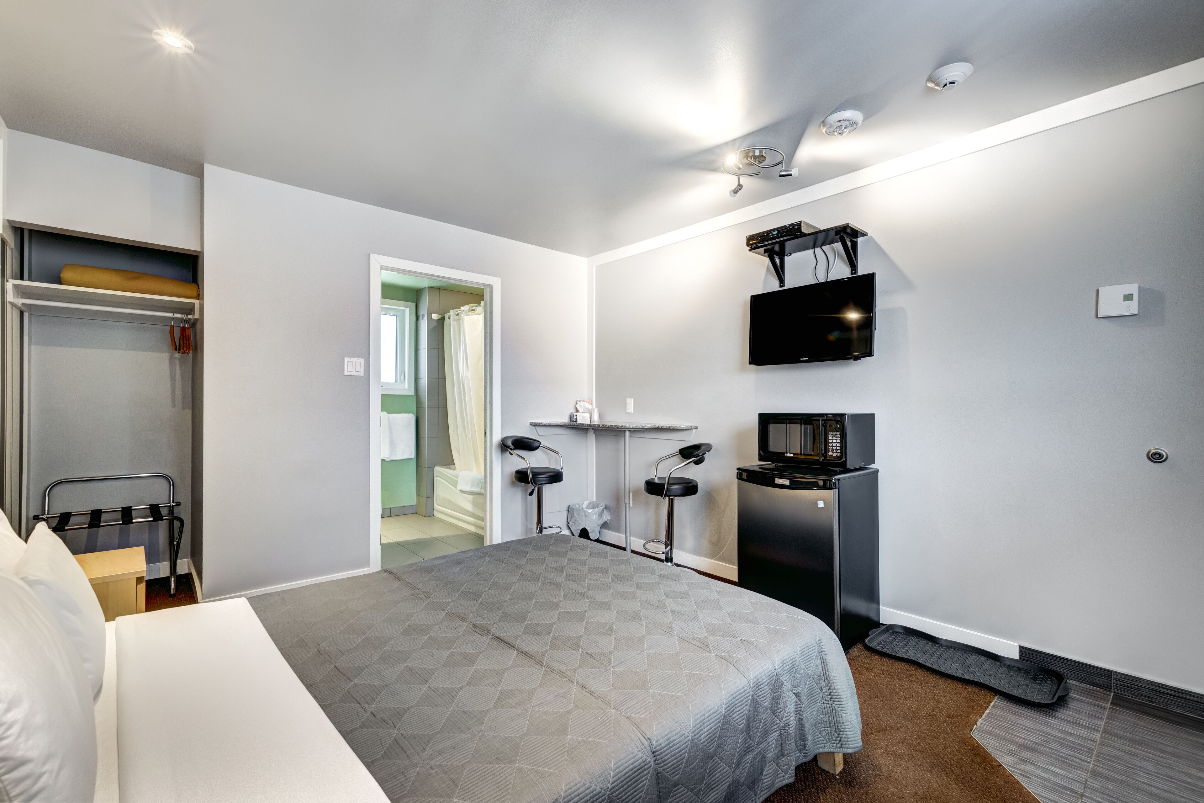 A modern hotel room with a bed, a desk, a TV, and a wardrobe.