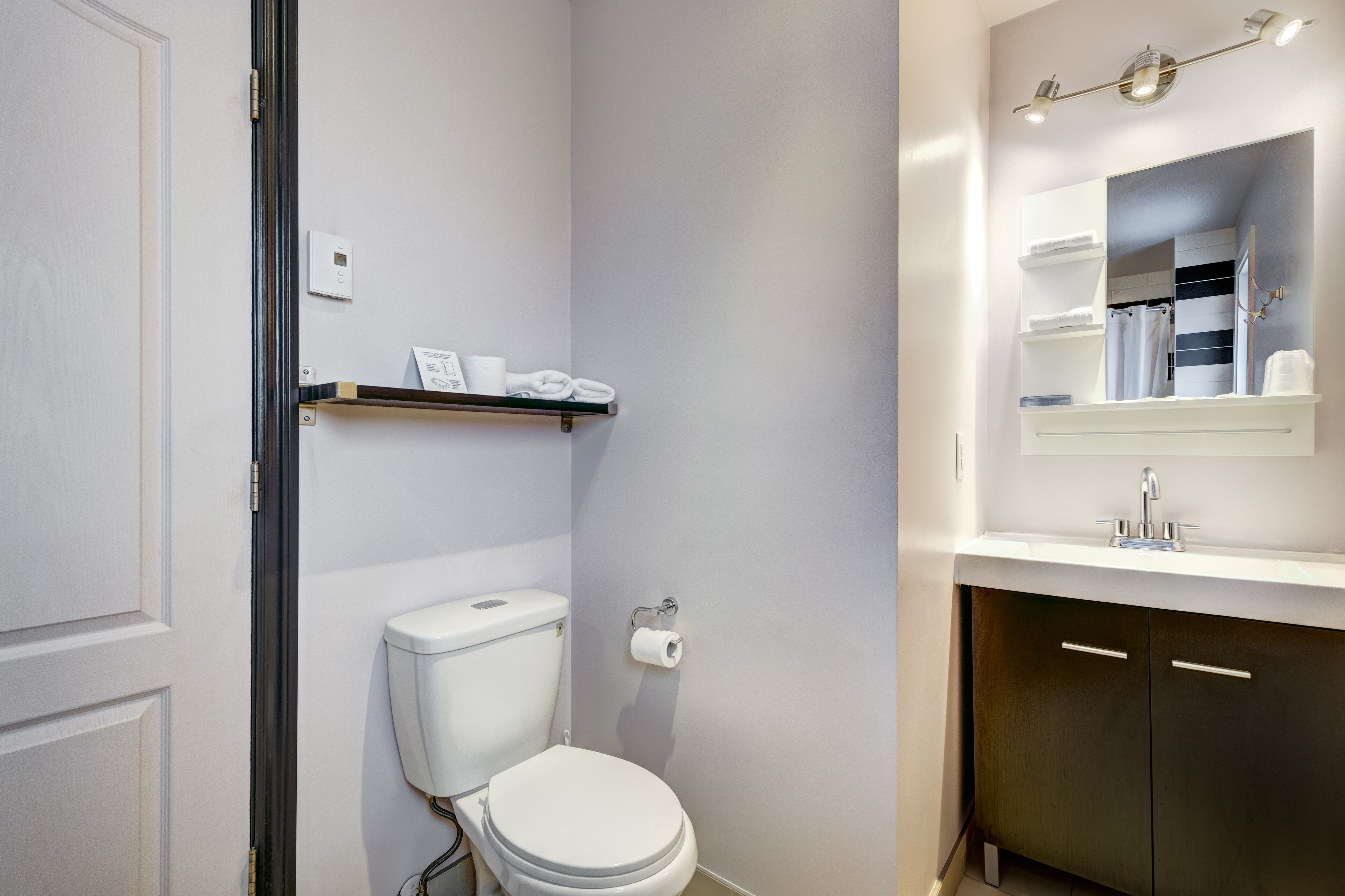 Een moderne badkamer met toilet, een plank met handdoeken, een spiegel en een wastafel.