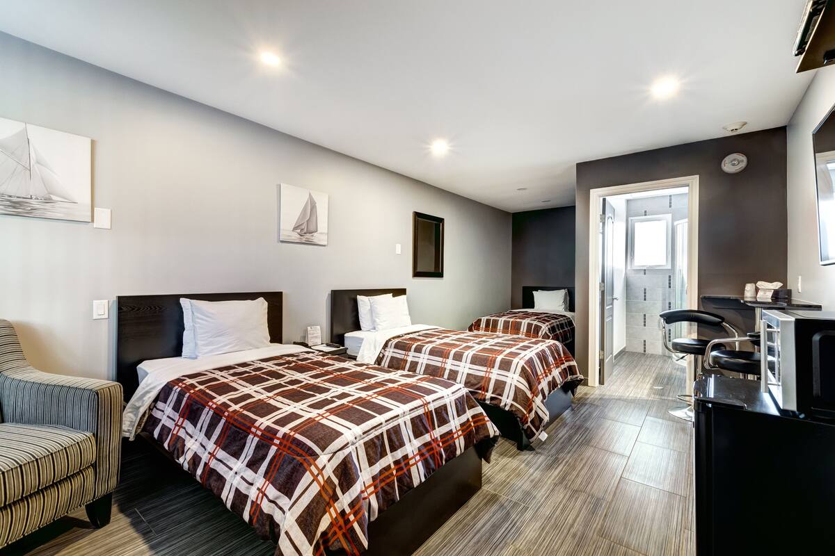 Habitación de hotel con dos camas, una silla, un escritorio y un kitchenette.