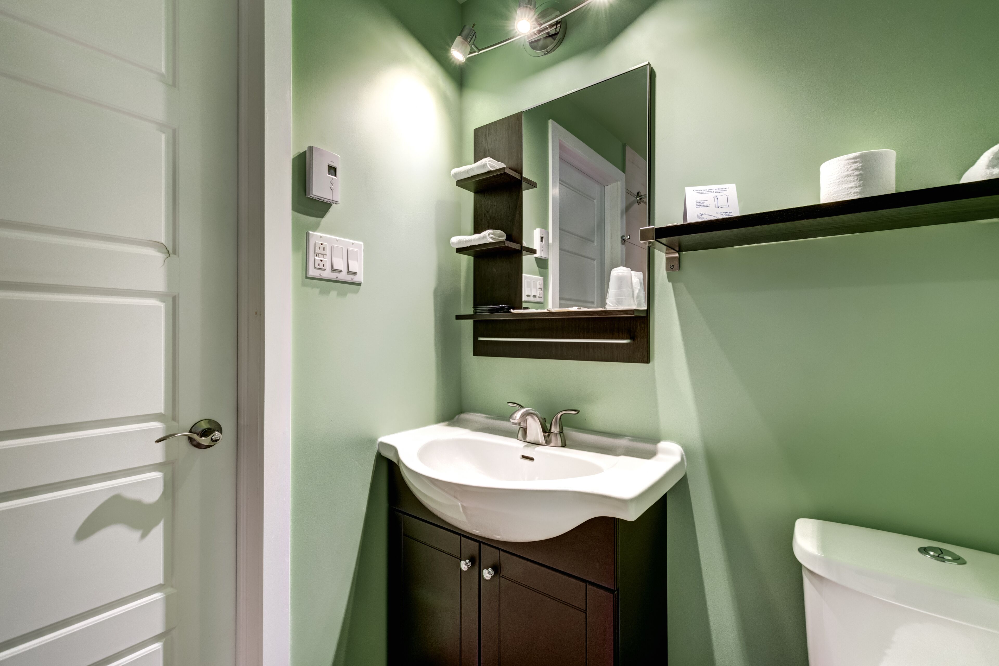 Un baño con lavamanos blanco, muebles oscuros, un espejo y un inodoro.