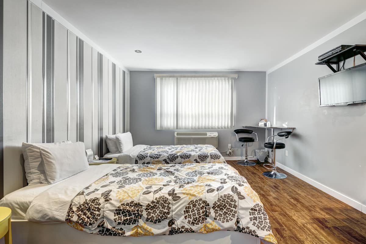 Una habitación de hotel con dos camas, un escritorio, una silla, un televisor y una ventana con persianas.