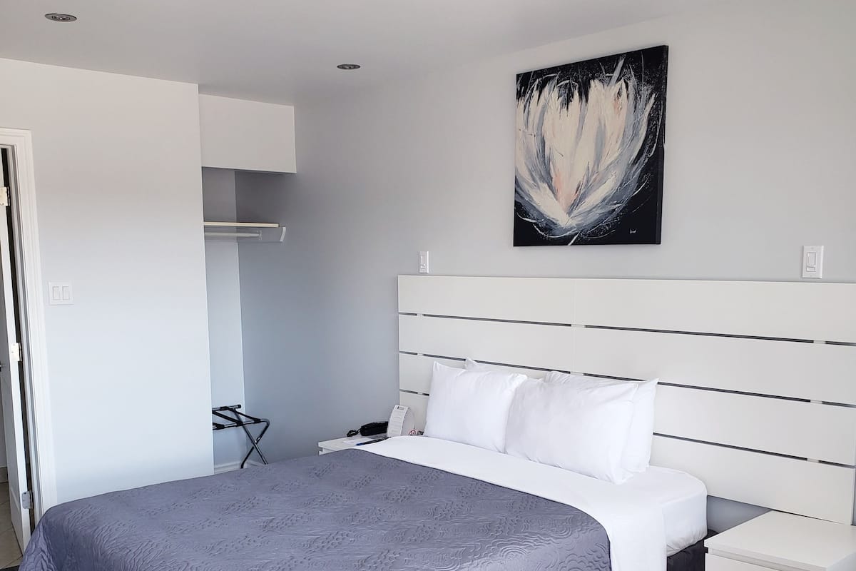 Un dormitorio moderno con una colcha gris estampada, almohadas blancas y una mesita de noche blanca.