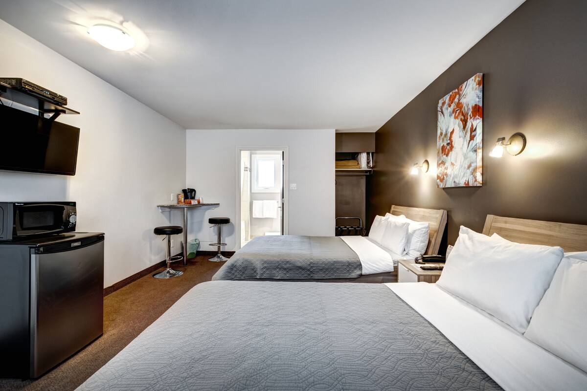 Habitación de hotel con dos camas, microondas, televisión, kitchenette pequeña y un cuadro en la pared.