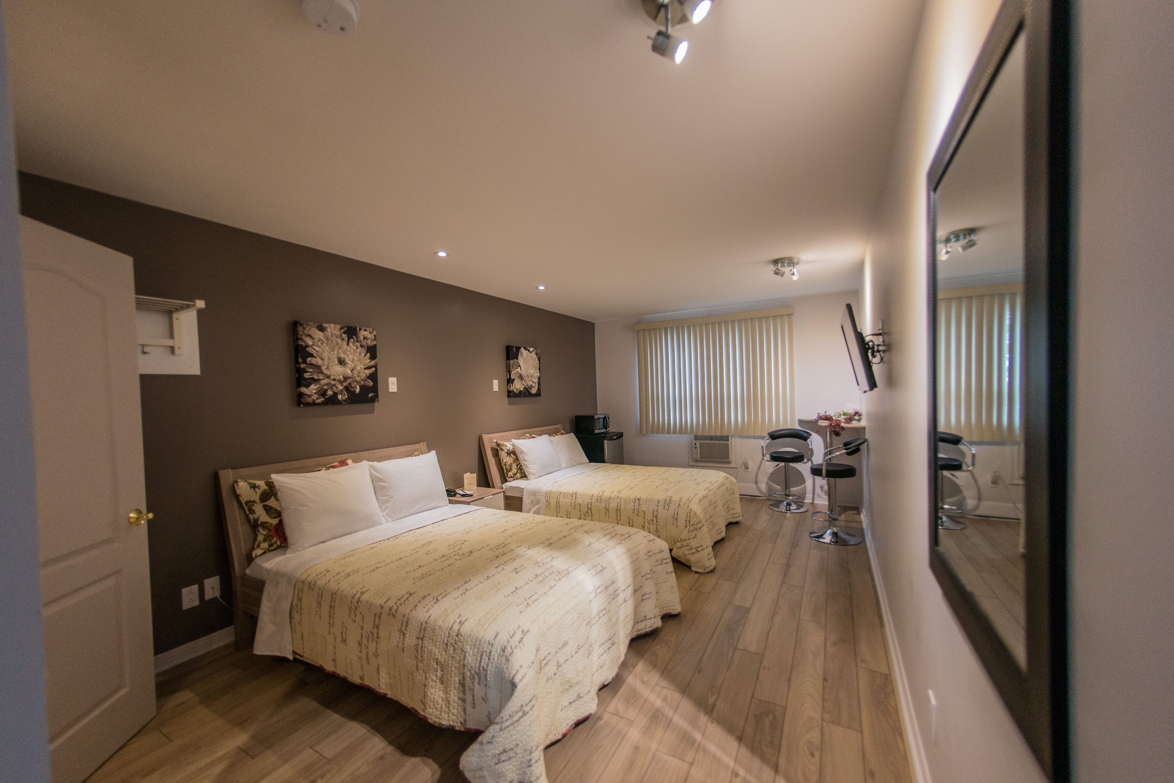 A hotel room with two beds, a desk with a chair, a mirror, and a window with blinds.