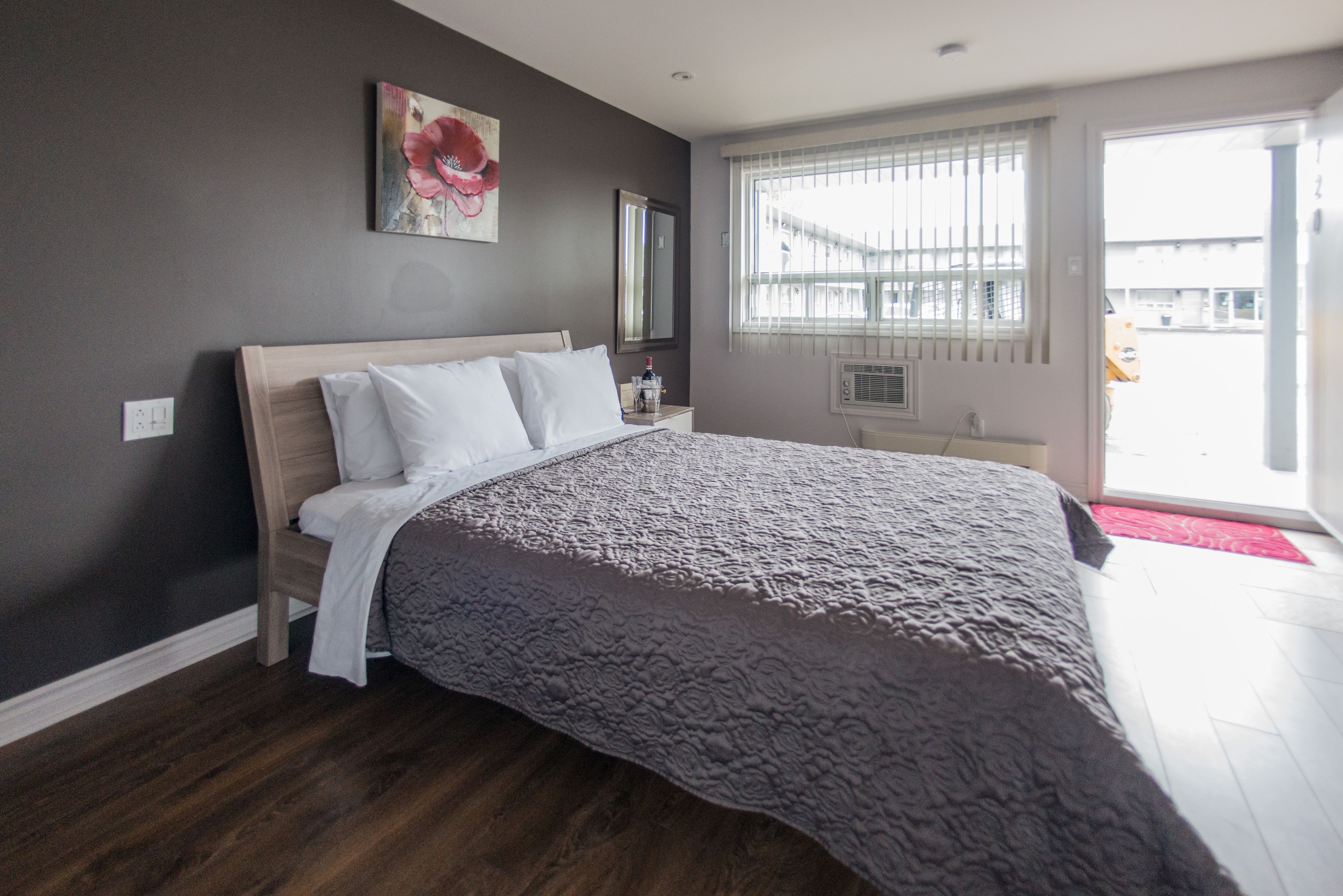 A bedroom with a large bed, a nightstand, a mirror, and a window with blinds.