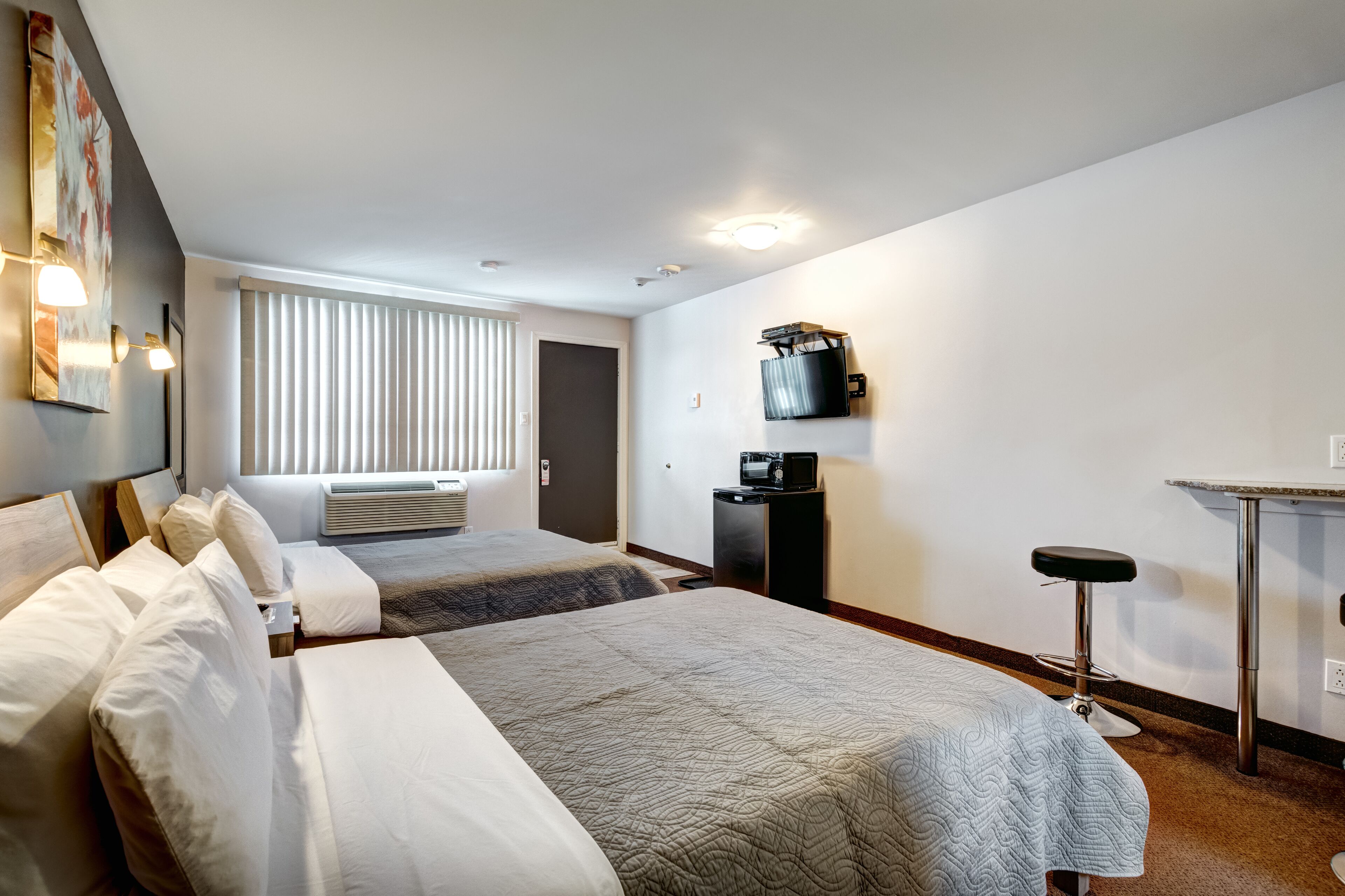 A hotel room with two beds, a desk, a chair, a TV, and a minibar.