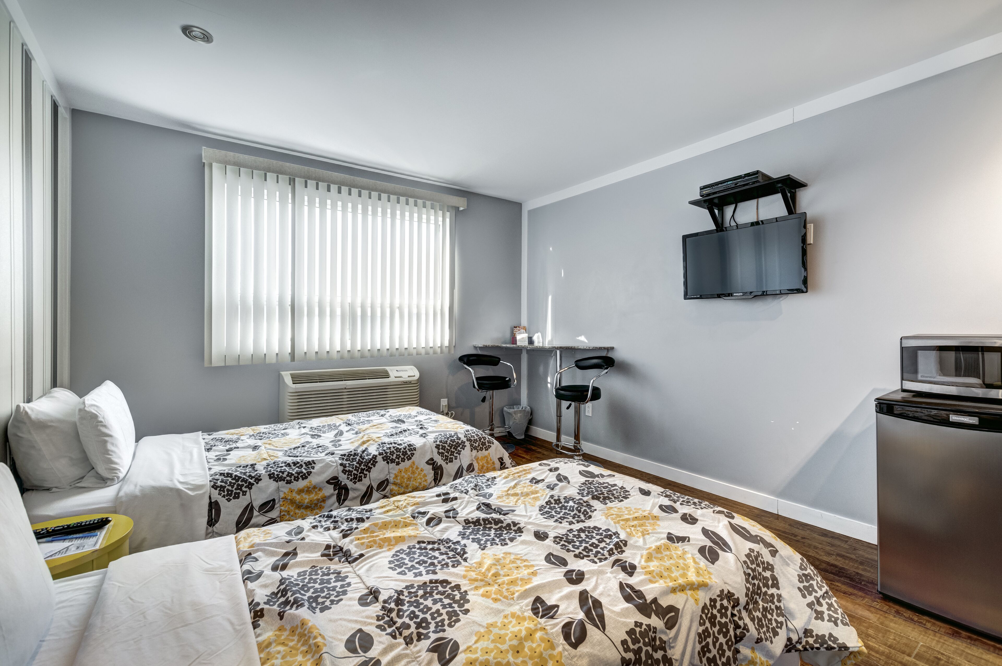 Une chambre d’hôtel avec deux lits, un téléviseur fixé au mur, un bureau avec une chaise et un réfrigérateur.