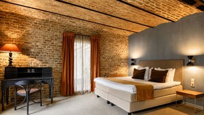 A bedroom with a brick wall, a bed with pillows, a desk with a lamp, and a window with curtains. - Hotel Winselerhof by Flow (Landgraaf)