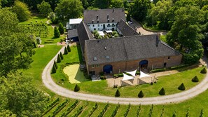 A large building with a brick exterior, surrounded by a well-maintained garden and a vineyard. - Hotel Winselerhof by Flow (Landgraaf)