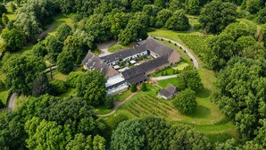 An aerial view of a large estate with multiple buildings, surrounded by dense greenery and a winding road. - Hotel Winselerhof by Flow (Landgraaf)