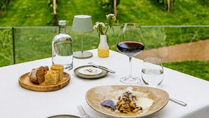 A table set outdoors with a vineyard view, featuring a wine glass, a bottle, and a plate of food. - Hotel Winselerhof by Flow (Landgraaf)