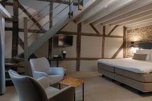 A modern bedroom with exposed beams, a flat-screen TV, a bed, and a seating area with a coffee table. - Hotel Winselerhof by Flow (Landgraaf)