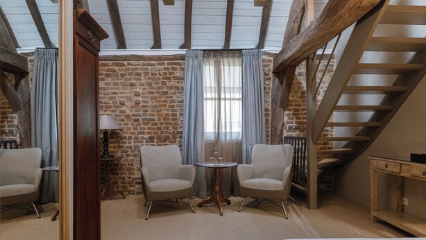 A cozy room with a brick wall, a wooden ceiling, a staircase, two chairs, a small table, and a bed. - Hotel Winselerhof by Flow (Landgraaf)