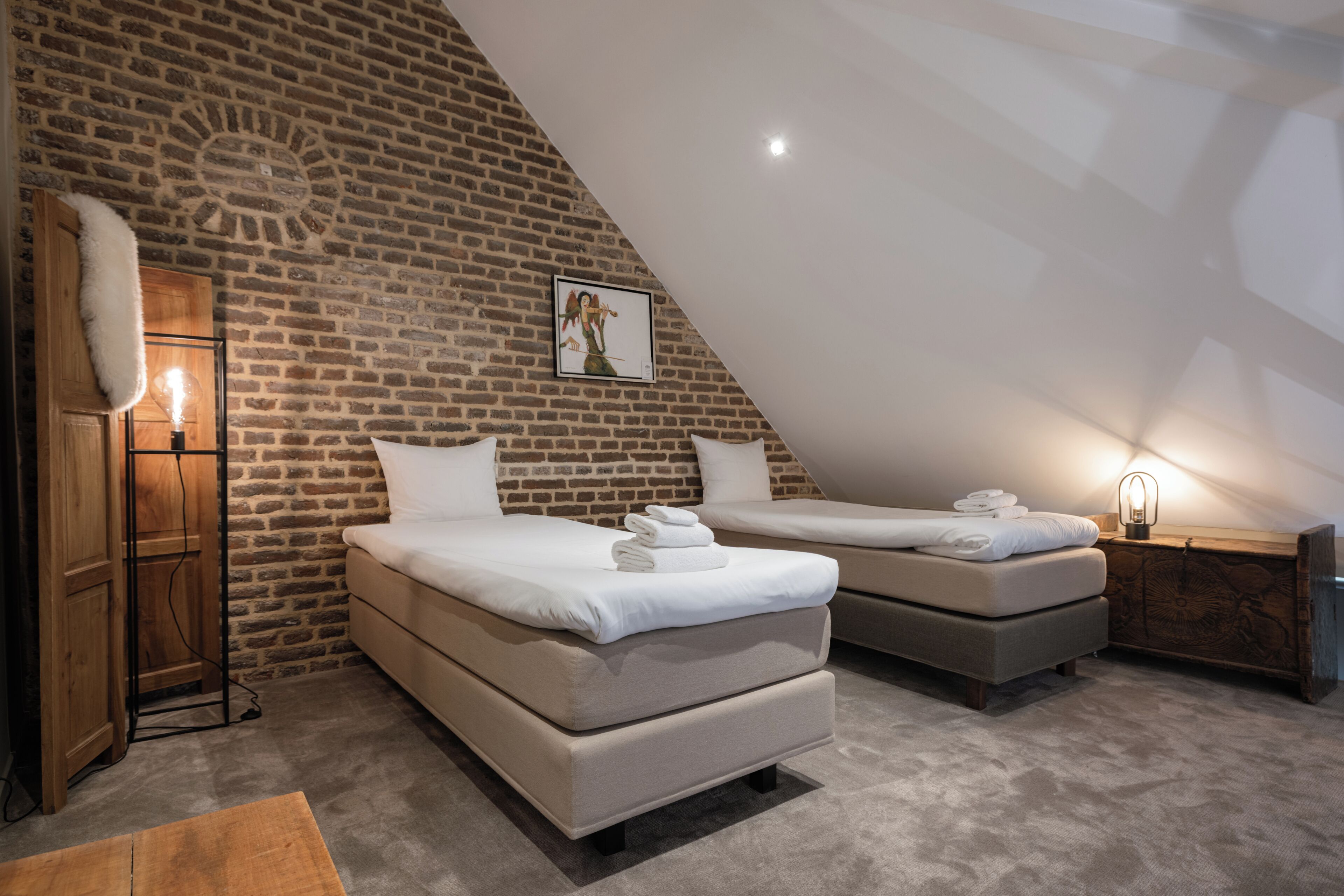 Un dormitorio con dos camas, una pared de ladrillo y un techo inclinado.