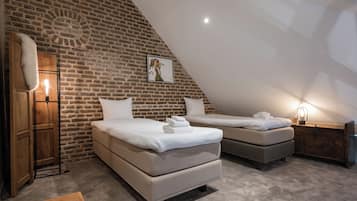 A bedroom with two beds, a brick wall, and a sloped ceiling.