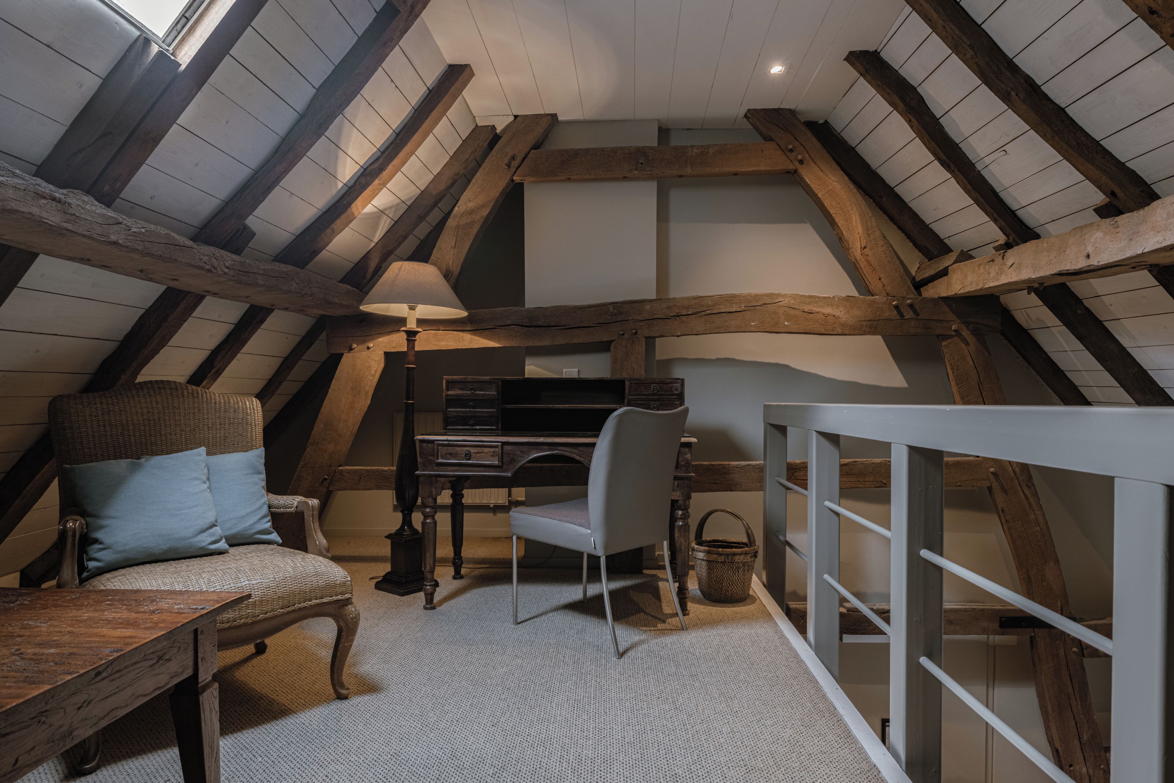 Acogedor dormitorio en ático con vigas de madera a la vista, un escritorio, una silla y un banco acolchado.