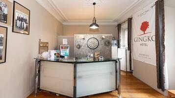 A hotel reception area with a glass counter, framed photographs on the wall, a clock, and a banner for the GINGKO HOTEL.