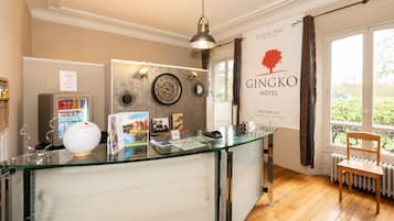 Un espace d’accueil avec un comptoir en verre, une horloge et une enseigne indiquant l’hôtel Gingko.