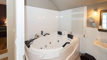 A modern bathroom with a large bathtub, white tiles, a wooden floor, and a small sink.