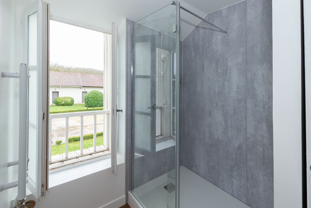 A modern bathroom with a glass shower enclosure, a large window, and a view of a green landscape.