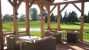 Een overdekt terras met rieten meubels en uitzicht op een golfbaan.