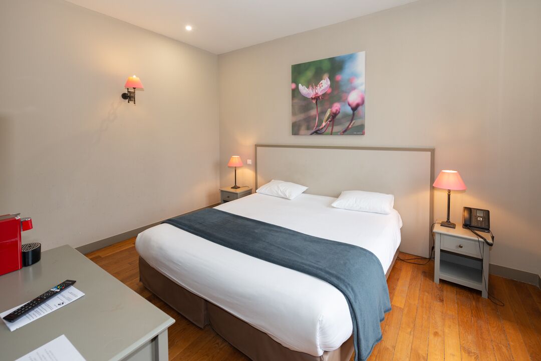 A hotel room with a large bed, bedside tables with lamps, a desk with a remote control, and a painting on the wall.