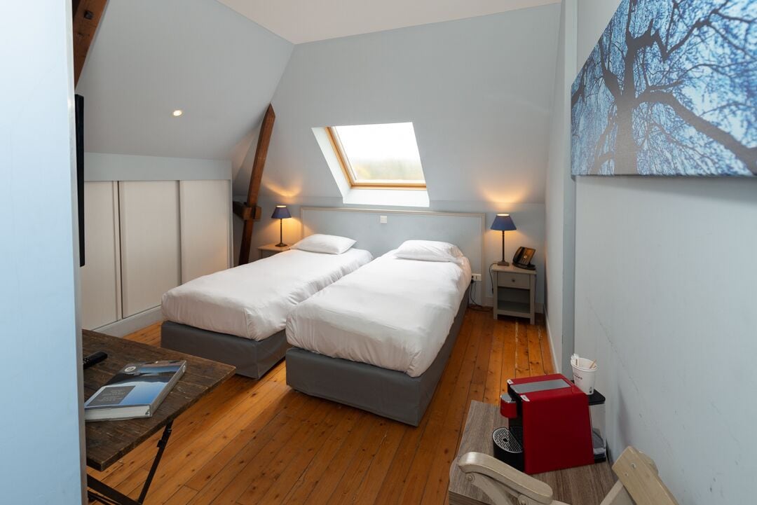 A room with two beds, a skylight, a table with a book, and a red box.