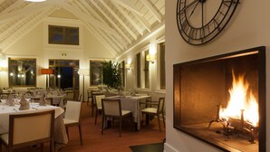Een eetgedeelte met getoonde tafels, een grote klok aan de muur en een open haard met vuur.