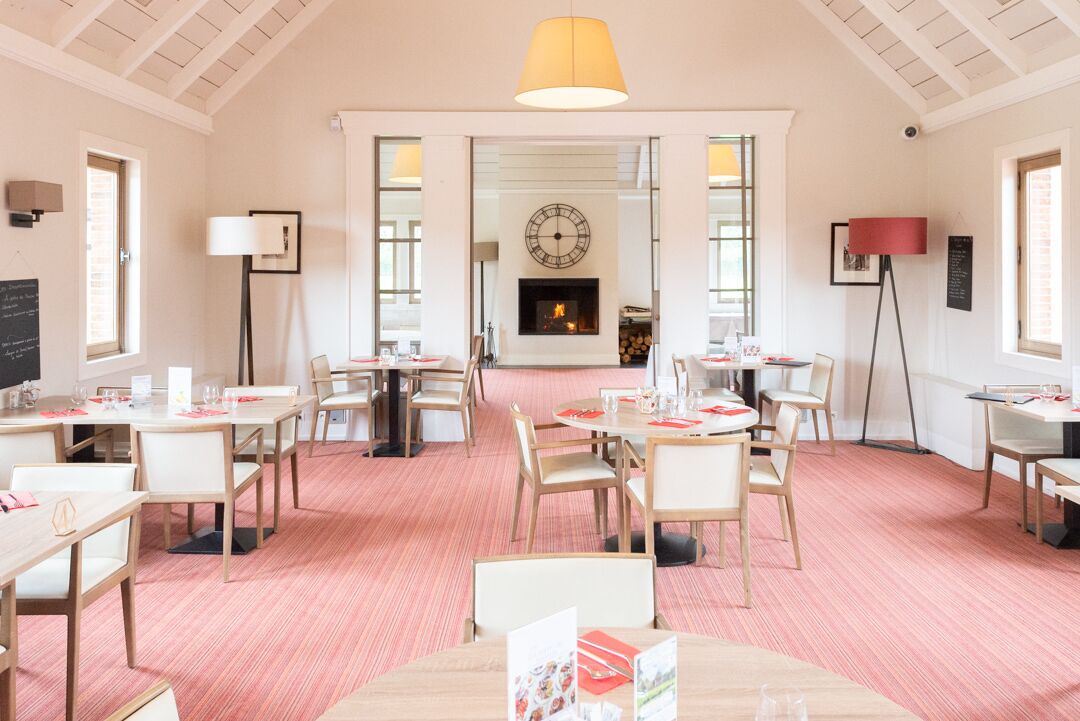 Une salle à manger d’hôtel avec plusieurs tables et chaises, une cheminée et une horloge au mur.