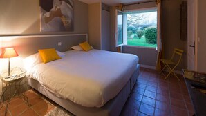 Een slaapkamer met een groot bed, een nachtkastje met lamp, een raam met uitzicht op groen en een stoel bij het raam.