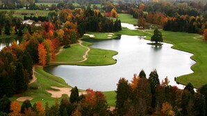 Een golfbaan met een meer, omgeven door bomen met herfstkleuren.
