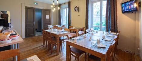 A dining area with wooden tables and chairs, a television mounted on the wall, and a clock on the wall.