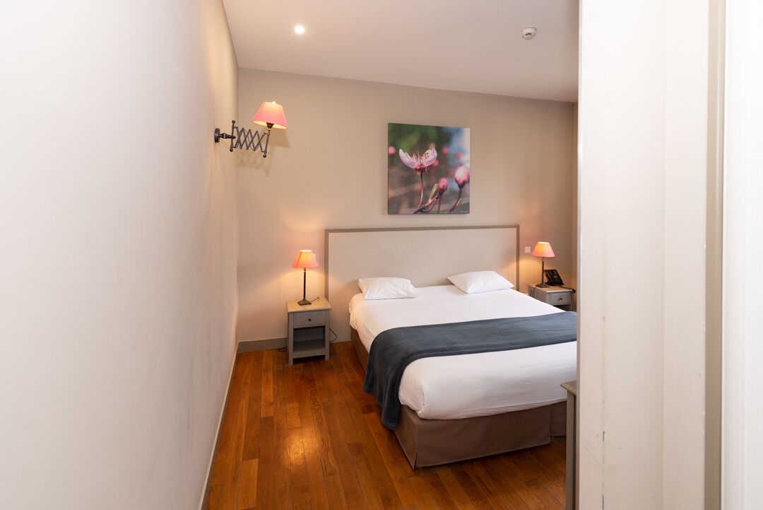 Un dormitorio con una cama, dos mesitas de noche, una lámpara de pared y un cuadro.