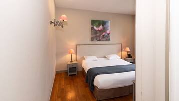 Un dormitorio con una cama, dos mesitas de noche, una lámpara de pared y un cuadro.