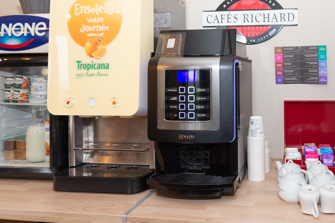 En kaffemaskine med digitalt display, en Tropicana juiceudskænker og en stak hvide kopper.