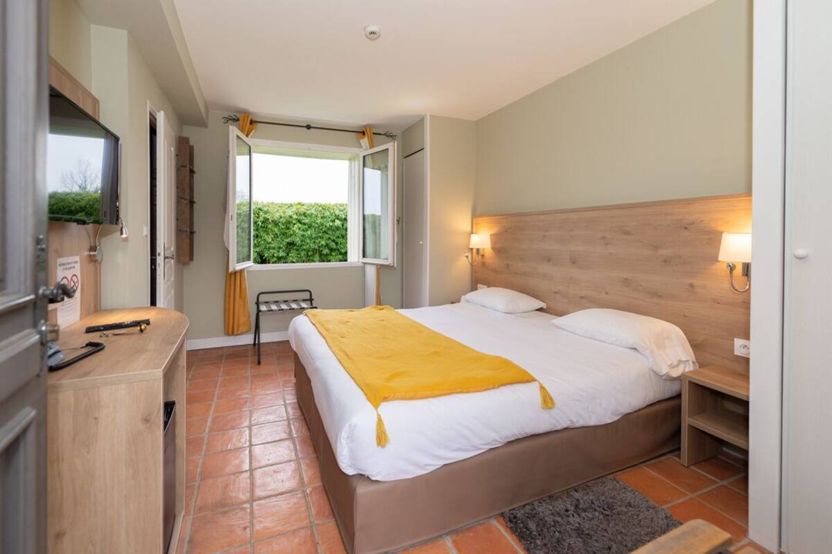 Een slaapkamer met een bed, bedlampjes, een raam en een bureau.