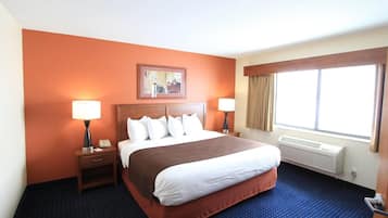A hotel room with a large bed, two bedside tables with lamps, a framed picture above the bed, a window with curtains, and a radiator under the window.