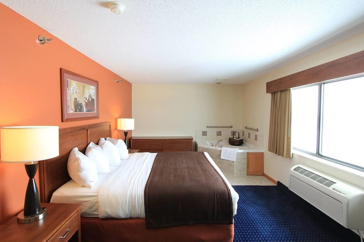 Ein Hotelzimmer mit Bett, Nachttischlampen, Schreibtisch, Badezimmer mit Badewanne und einem großen Fenster.