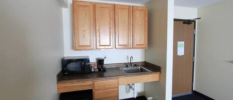 A compact kitchenette with wooden cabinets, a microwave, a coffee maker, and a sink.