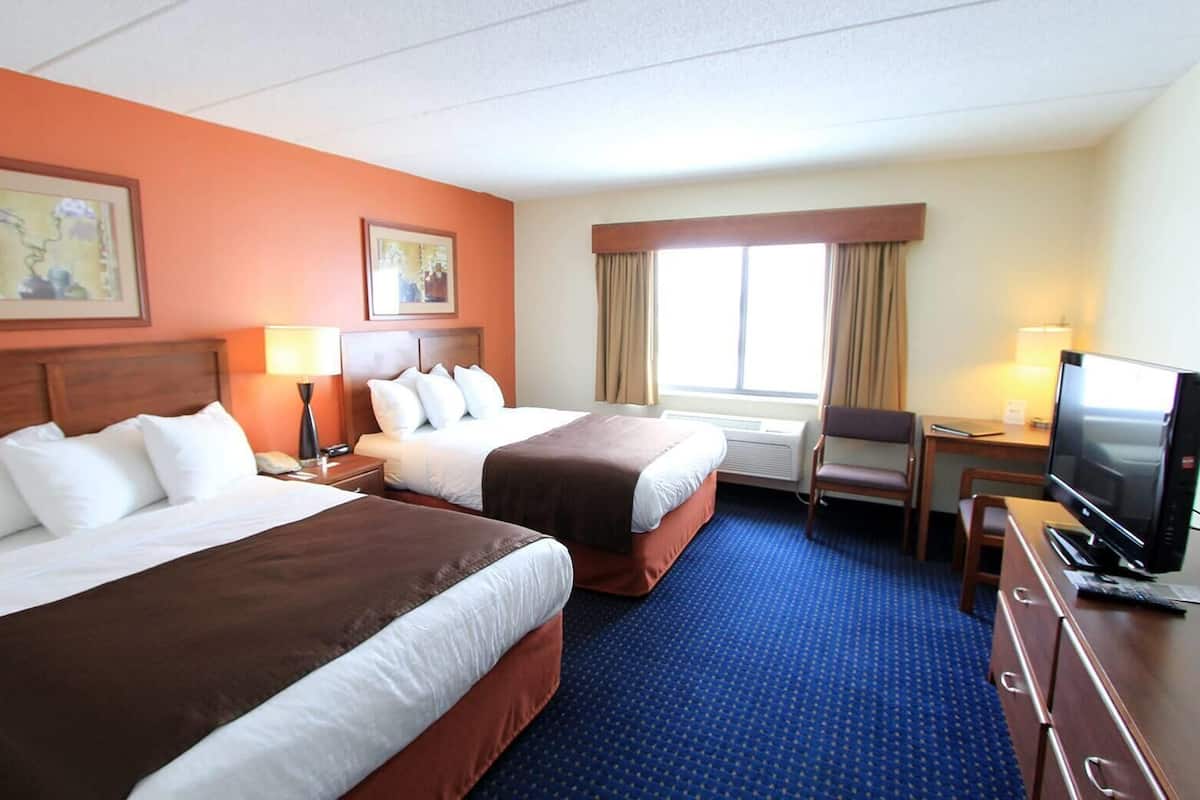 Ein Hotelzimmer mit zwei Betten, einem Schreibtisch, einem Fernseher und einem Stuhl.