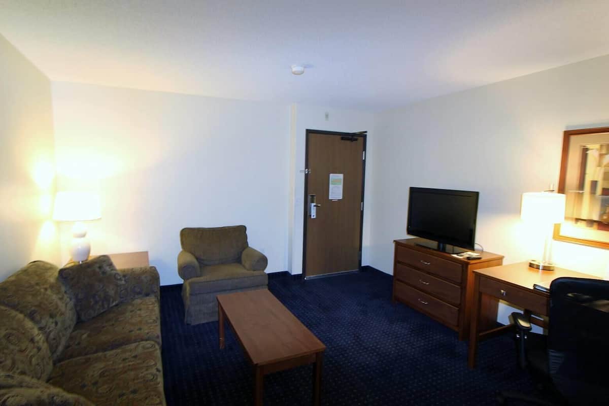Ein Hotelzimmer mit Sofa, Sessel, Schreibtisch, Fernseher und einer Tür.