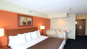 Habitación de hotel con cama, baño con bañera, un cuadro en la pared y una puerta.