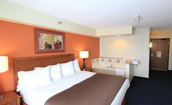 A hotel room with a bed, a bathroom with a bathtub, a painting on the wall, and a door.