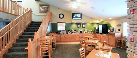 A restaurant with wooden furniture, a kitchen area, and a staircase.