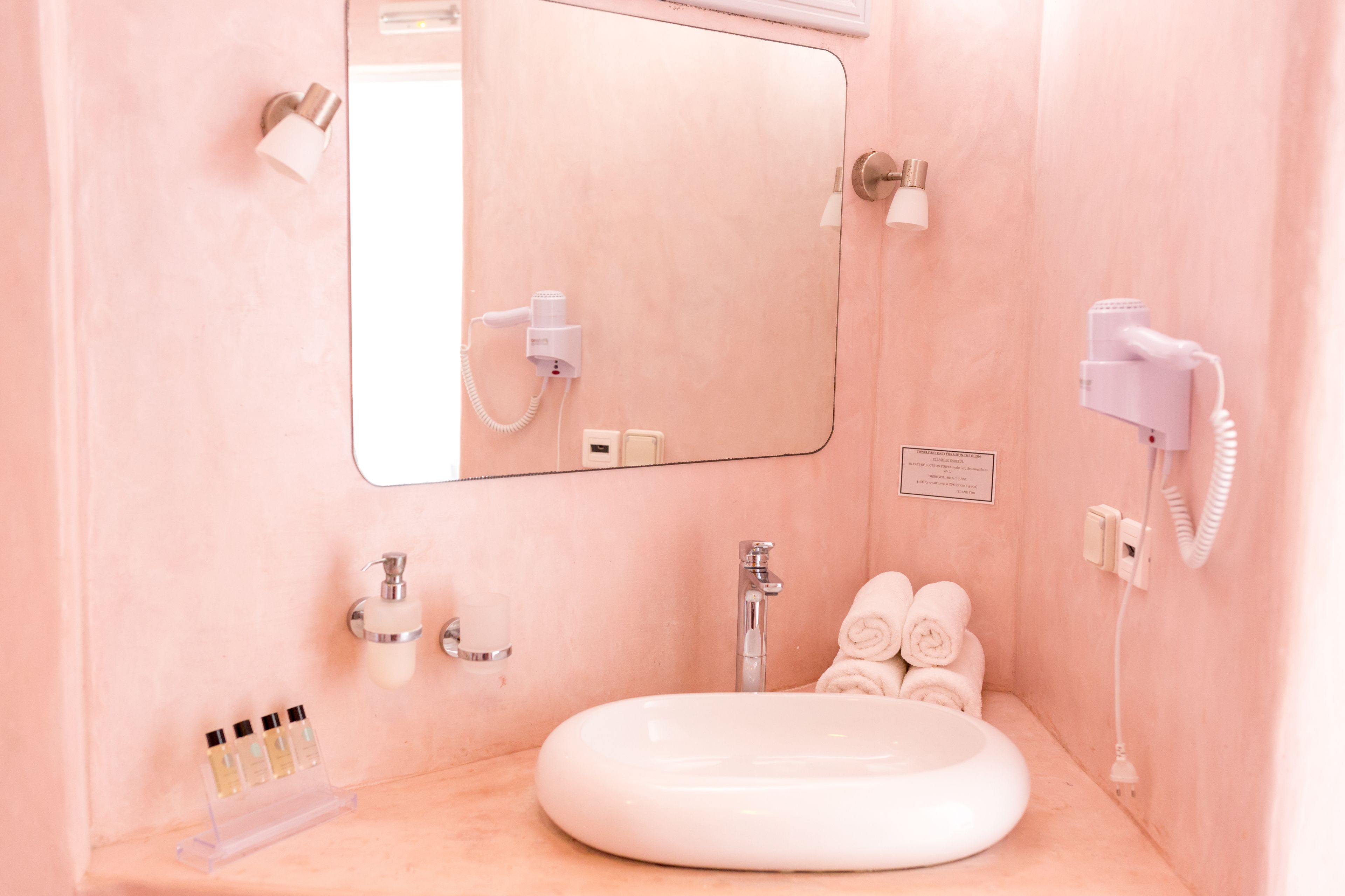 A pink bathroom with a white sink, a mirror, a hairdryer, and a towel rack.