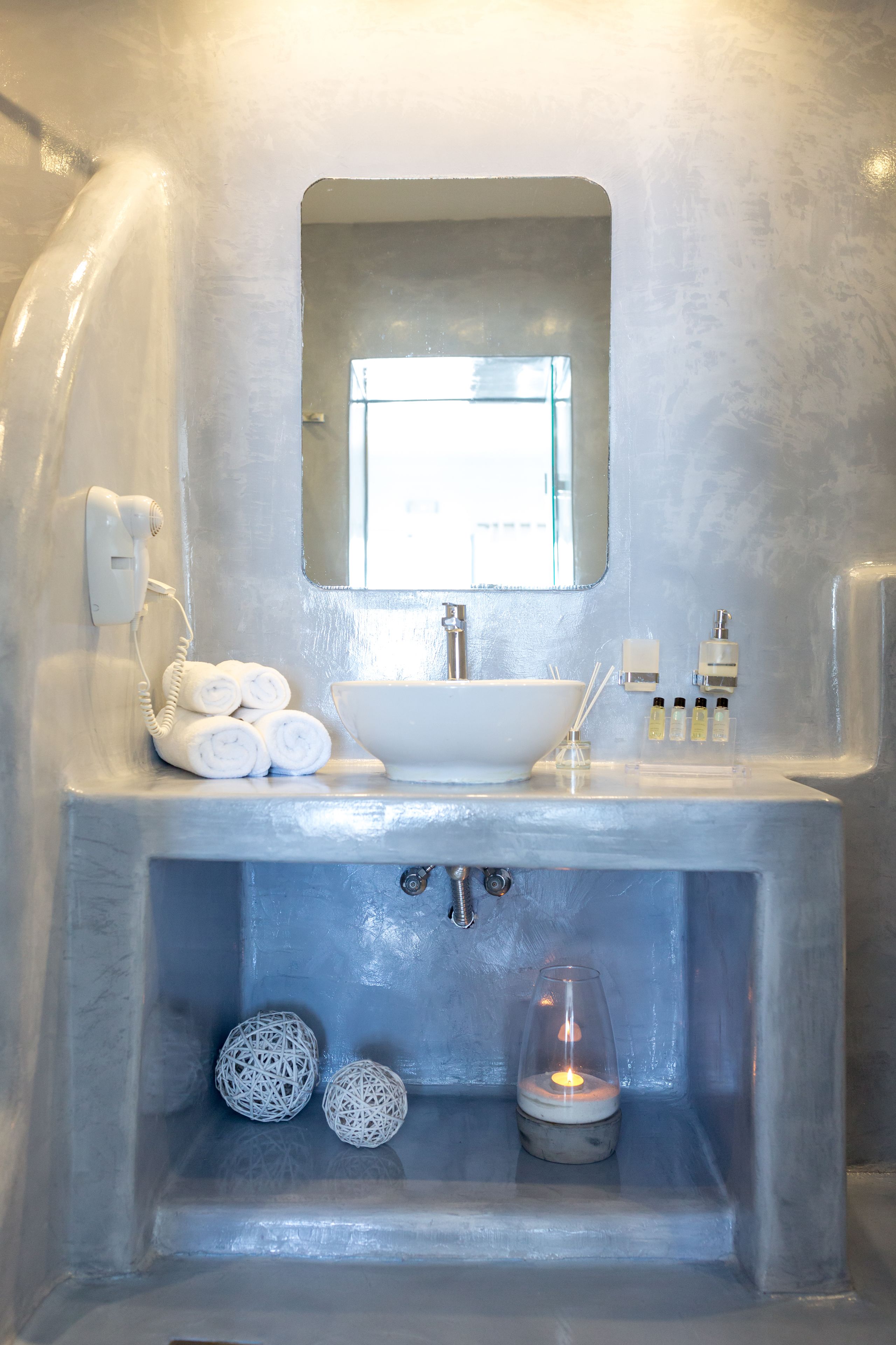 Un baño con un lavabo blanco, un espejo, un teléfono y dos adornos decorativos.