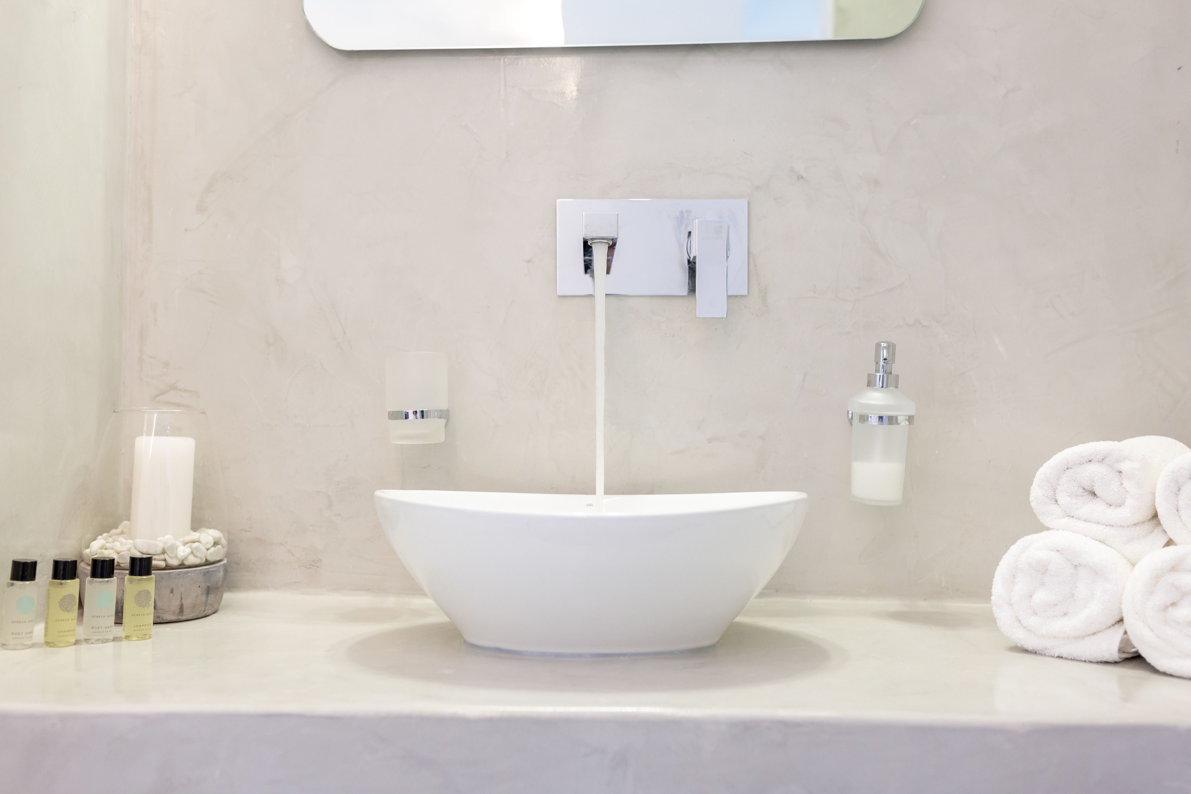 A bathroom with a white vessel sink, a mirror above it, and a towel rack with rolled towels.