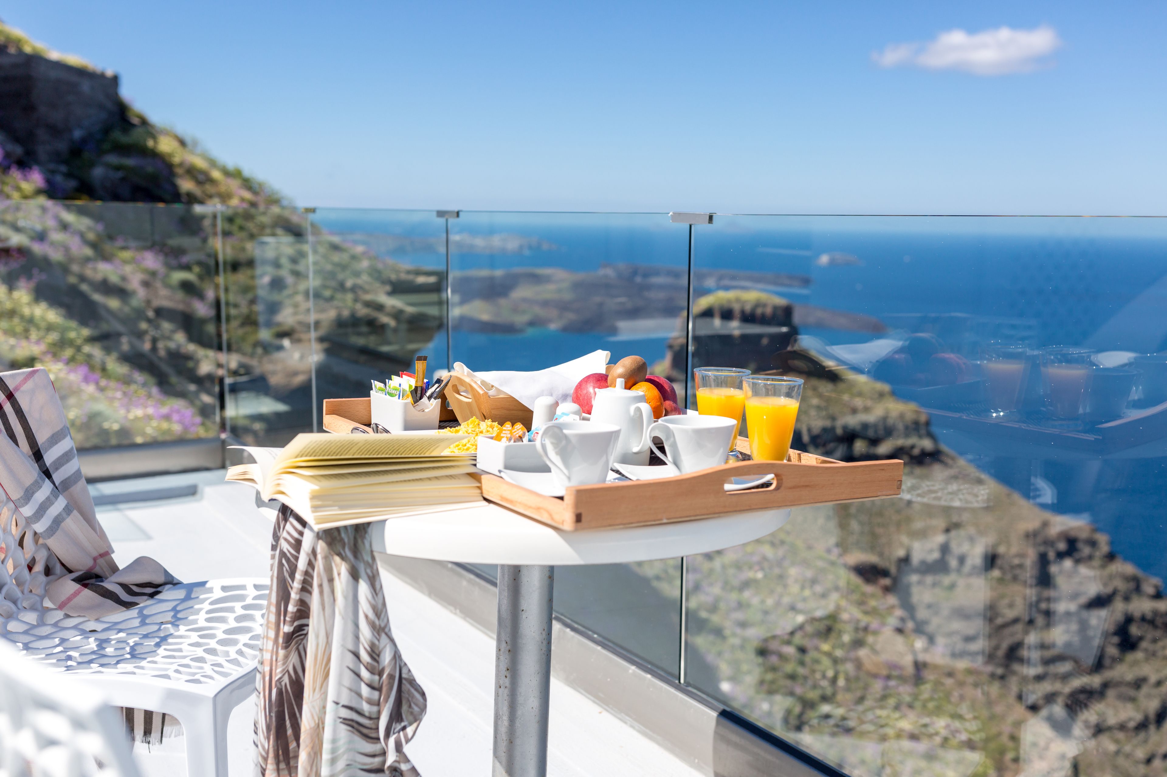 Bandeja de desayuno con comida y bebidas en un balcón con vistas a un paisaje costero.